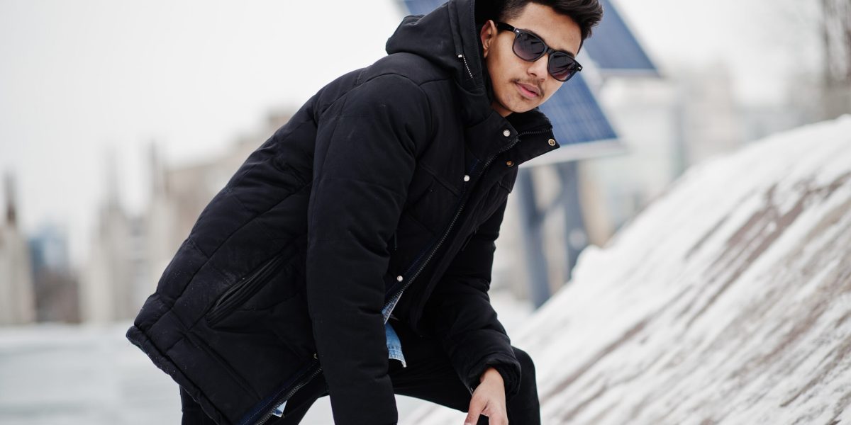 Casual young indian man in black jacket and sunglasses posed at winter day.